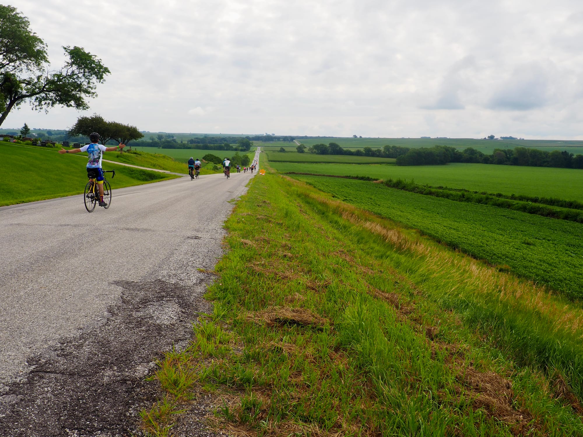 Cyclists heading down a hill. One person has their arms outstretched into a T shape.