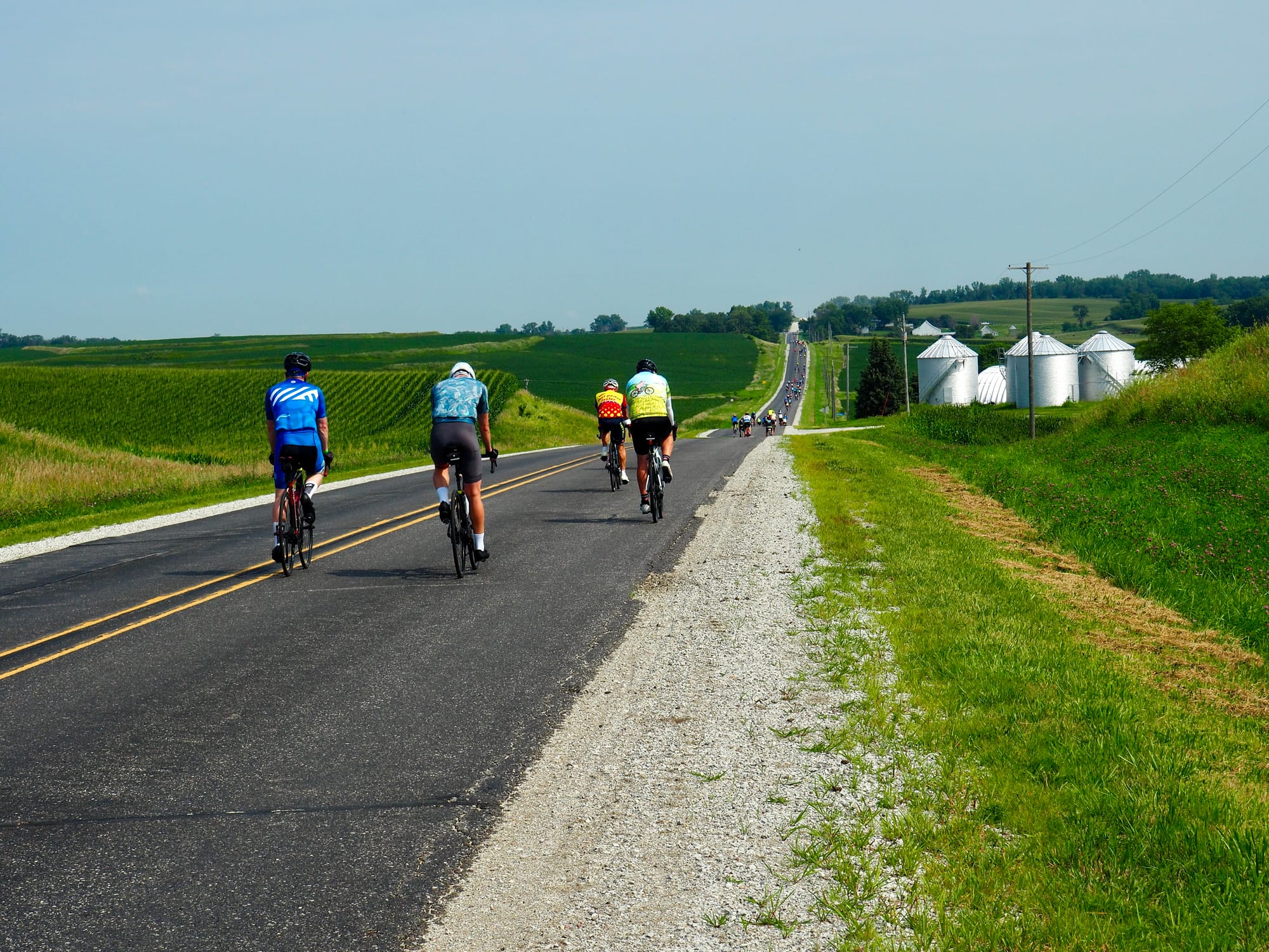 Cyclists heading down a hill with grain silos on the right.